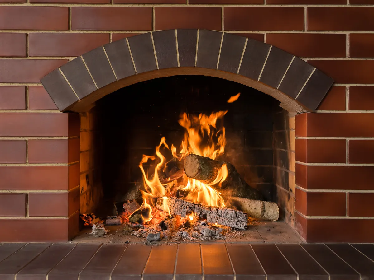 A wood fire burning in a red brick fireplace with an arched opening and a tiled hearth.